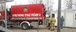 Samochód transportowy PSP, z którego strażacy wyładowują środki ochrony indywidualnej.