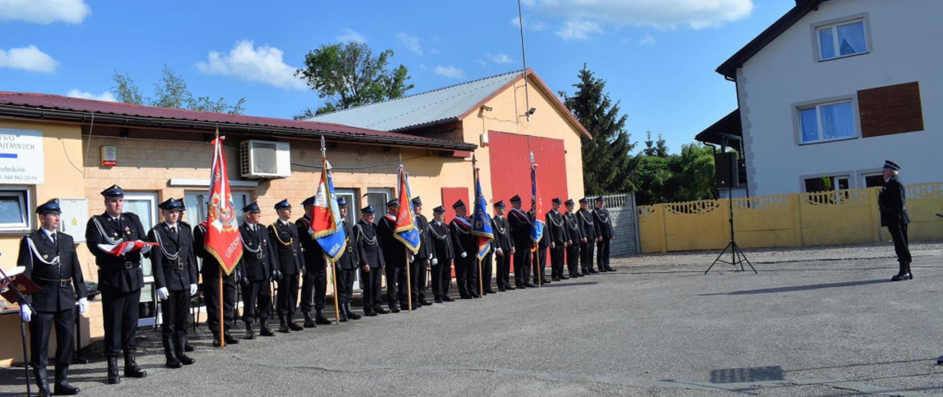 Na zdjęciu widoczne poczty sztandarowe stojące w szeregu przed budynkiem OSP Giżyce.