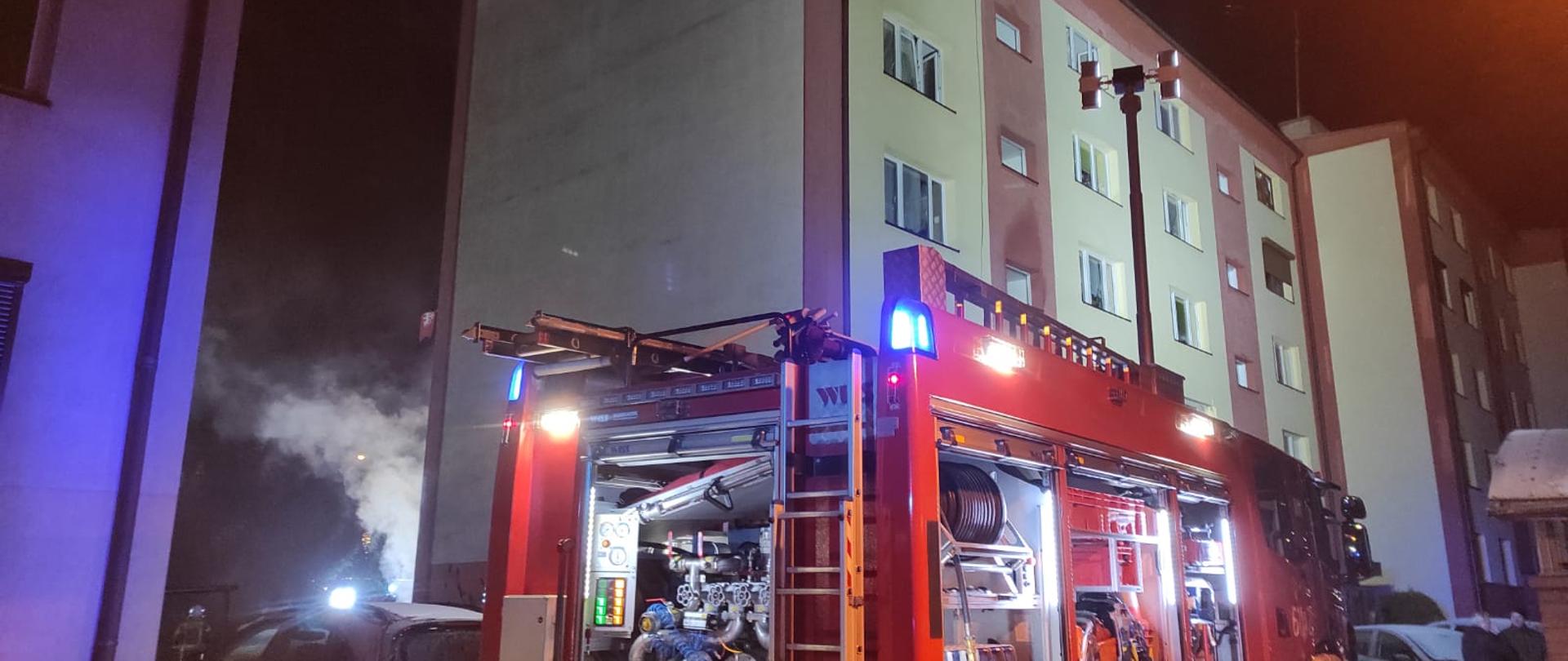 Na zdjęciu widać wóz strażacki obok bloku, z którego wydobywa się dym