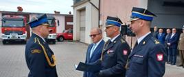 Zdjęcie przedstawia moment wręczania aktu nadania wyższego stopnia służbowego przez Zastępcę Komendanta Wojewódzkiego PSP w Toruniu w asyście komendanta Powiatowego i Senatora RP