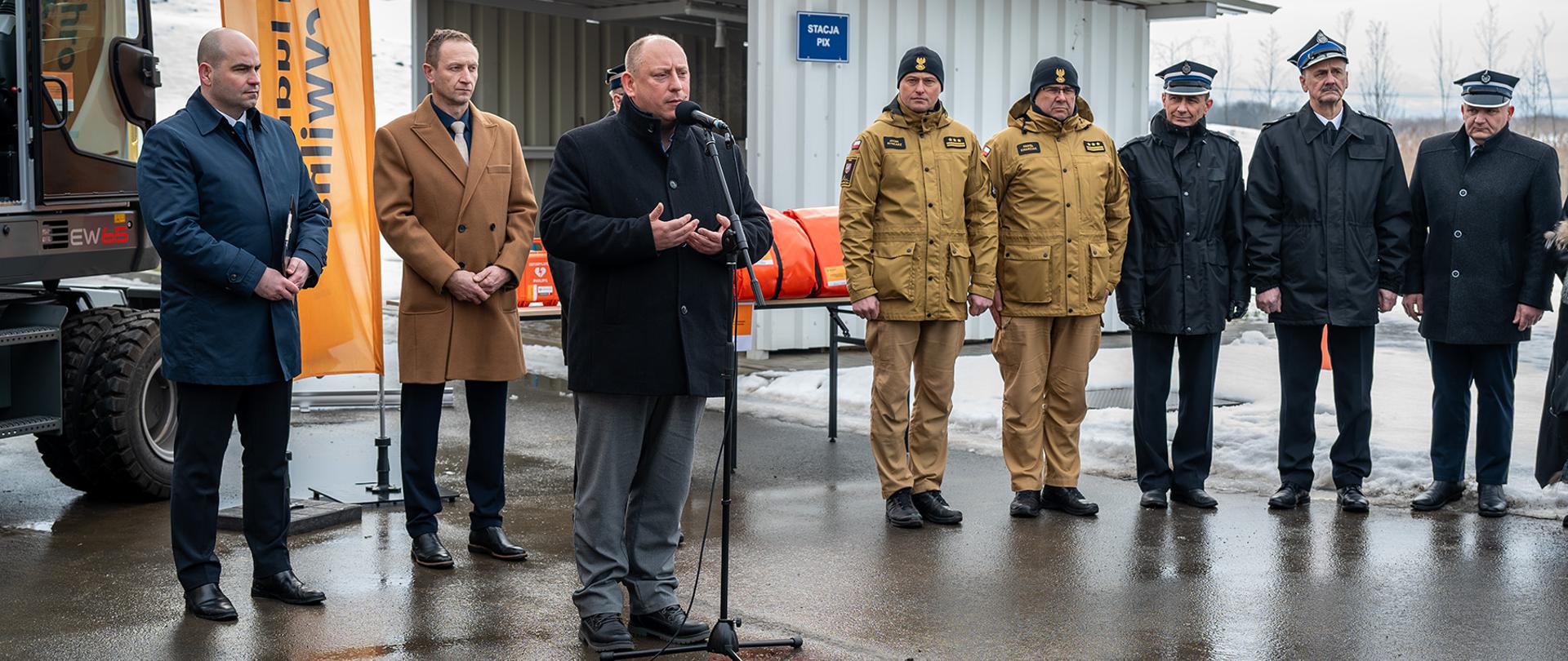 Na zdjęciu widać przemawiającego wojewodę małopolskiego. Za nim w rzędzie stoją przedstawiciele lokalnych władz, Państwowej Straży Pożarnej oraz Ochotniczych Straży Pożarnych.