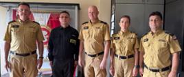 Na pierwszym planie, od lewej: Komendant Powiatowy PSP w Rypinie bryg. Piotr Wypych, sekc. Dawid Dąbrowski w czarnym ubraniu specjalnym strażaka, Zastępca Komendanta Powiatowego PSP w Rypinie kpt. Marcin Czarnecki, mł. asp. Justyna Pilśniak oraz kpt. Dariusz Kuciński. W tle widoczny jest sztandar Komendy Powiatowej Państwowej Straży Pożarnej w Rypinie.
