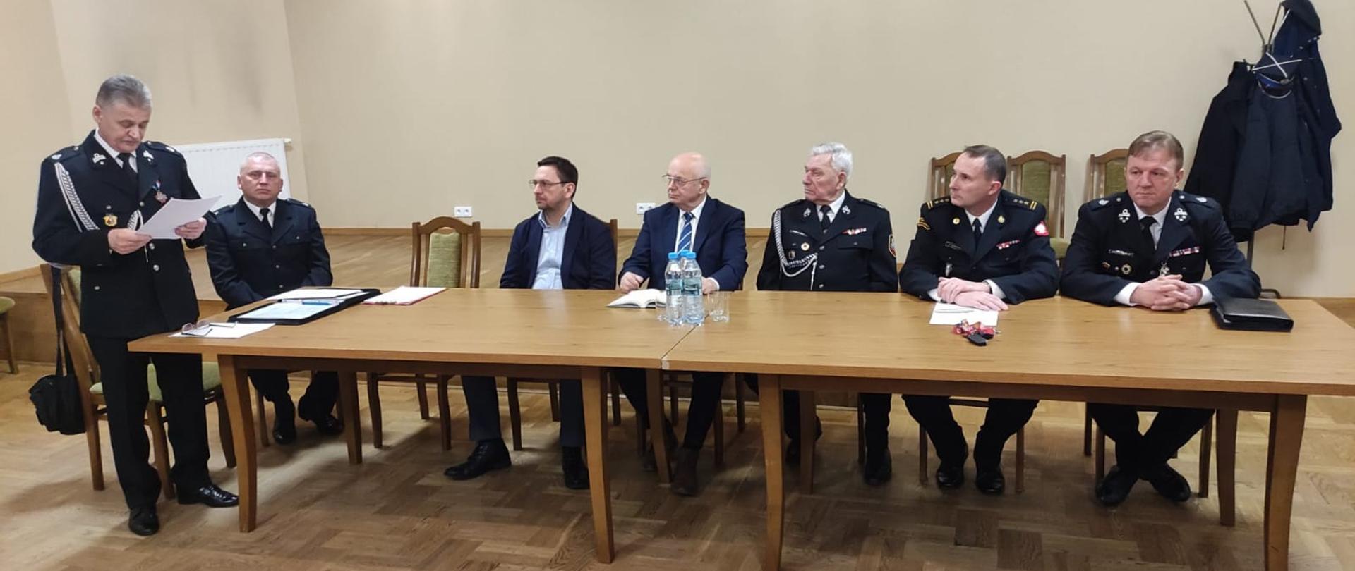 Zdjęcie przedstawia organizatorów i gości siedzący przy stole podczas spotkania sprawozdawczego Ochotniczej Straży Pożarnej w Woli Morawickiej.