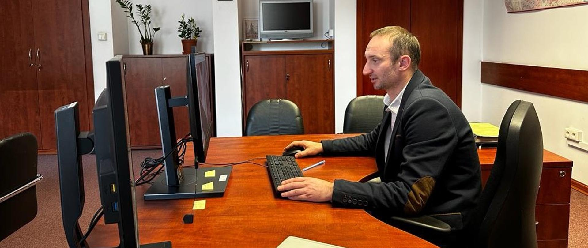 Osoba siedząca przy biurku w biurze, pracująca na komputerze.