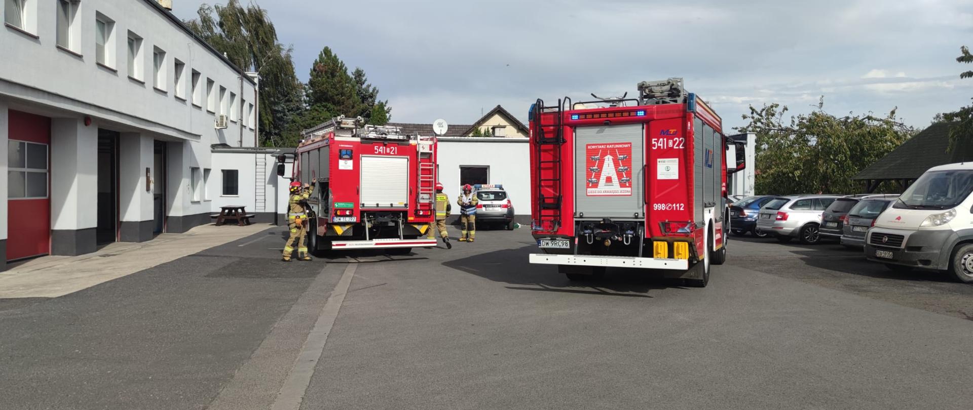 Samochody pożarnicze na tle budynku.