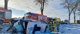 NA zdjęciu widać przewróconą karetkę, ratowników oraz wozy służb ratunkowych 