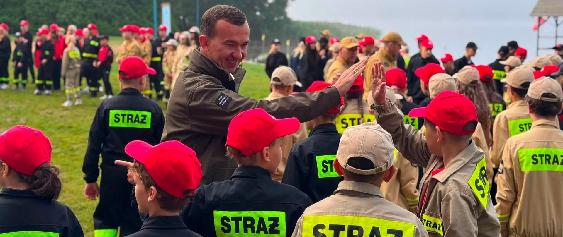 kilkanaście młodych osób w mundurze strażaka stoi i przybija piątkę mężczyźnie 