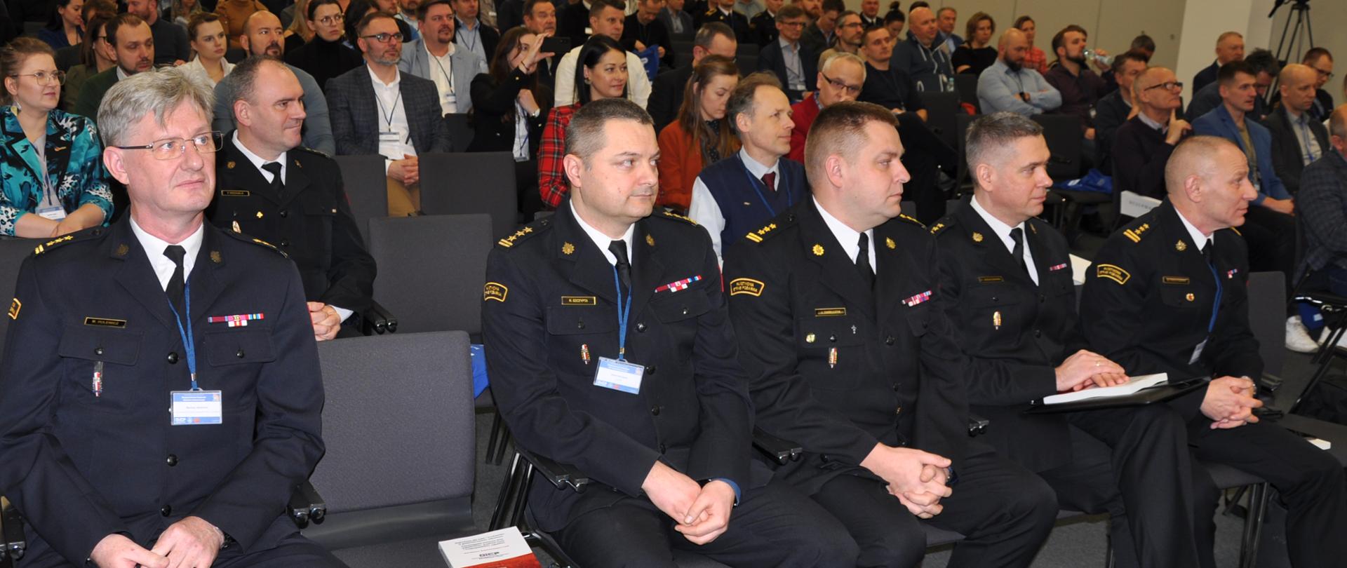 konfernecja, w dużej sali w pierwsyzm rzędzie siedzą strażacy, w kolejnych rzędach inni słuchacze