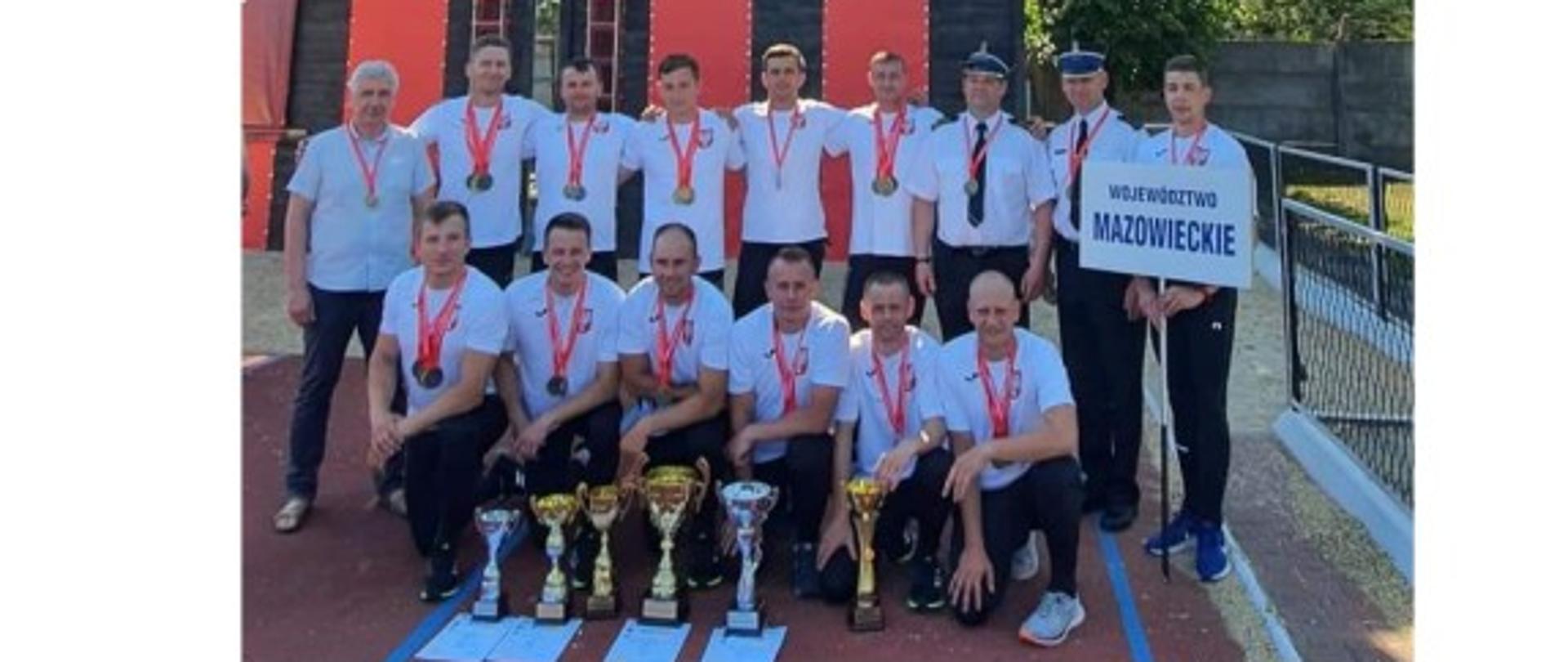 zdjęcie grupowe kadry województwa mazowieckiego w sporcie pożarniczym na tle wspinalnie, przez zawodnikami na tartanie puchary i dyplomy