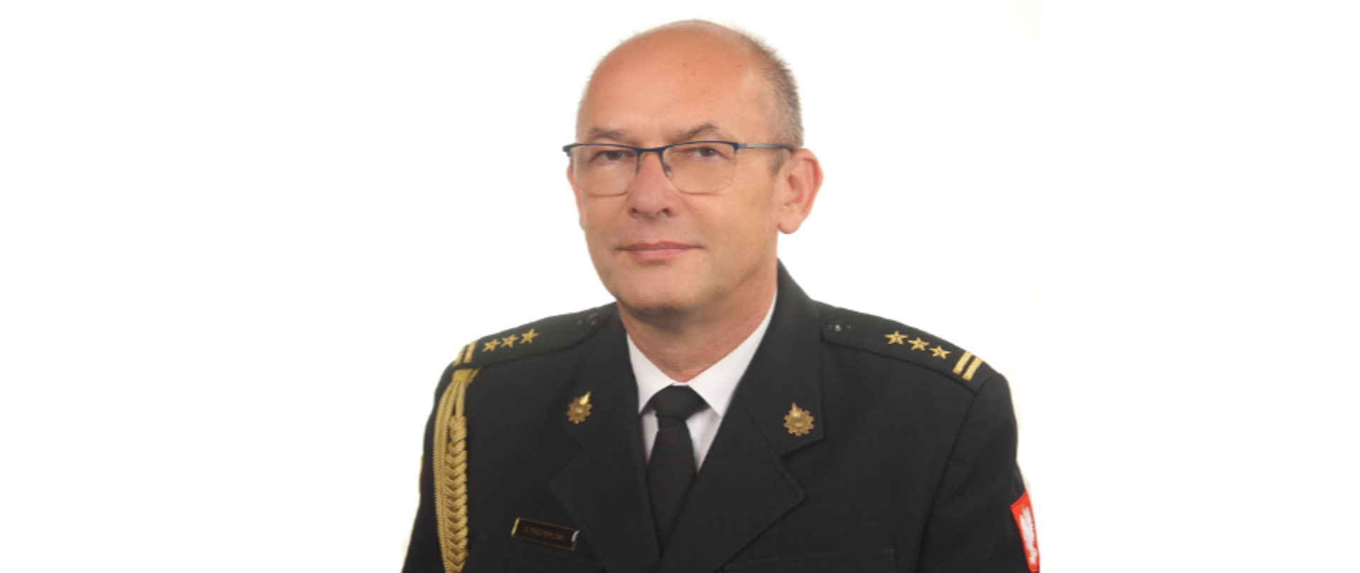 Oficer PSP w mundurze galowym, bez czapki. Ma okulary.