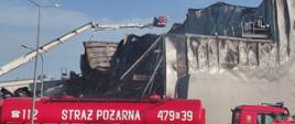 Cysterna pożarnicza GCBA 479[G]39 i podnośnik SHD z koszem prowadzący działania gaśnicze na zniszczonym dachu hali; ściany obiektu stopione od wysokiej temperatury.