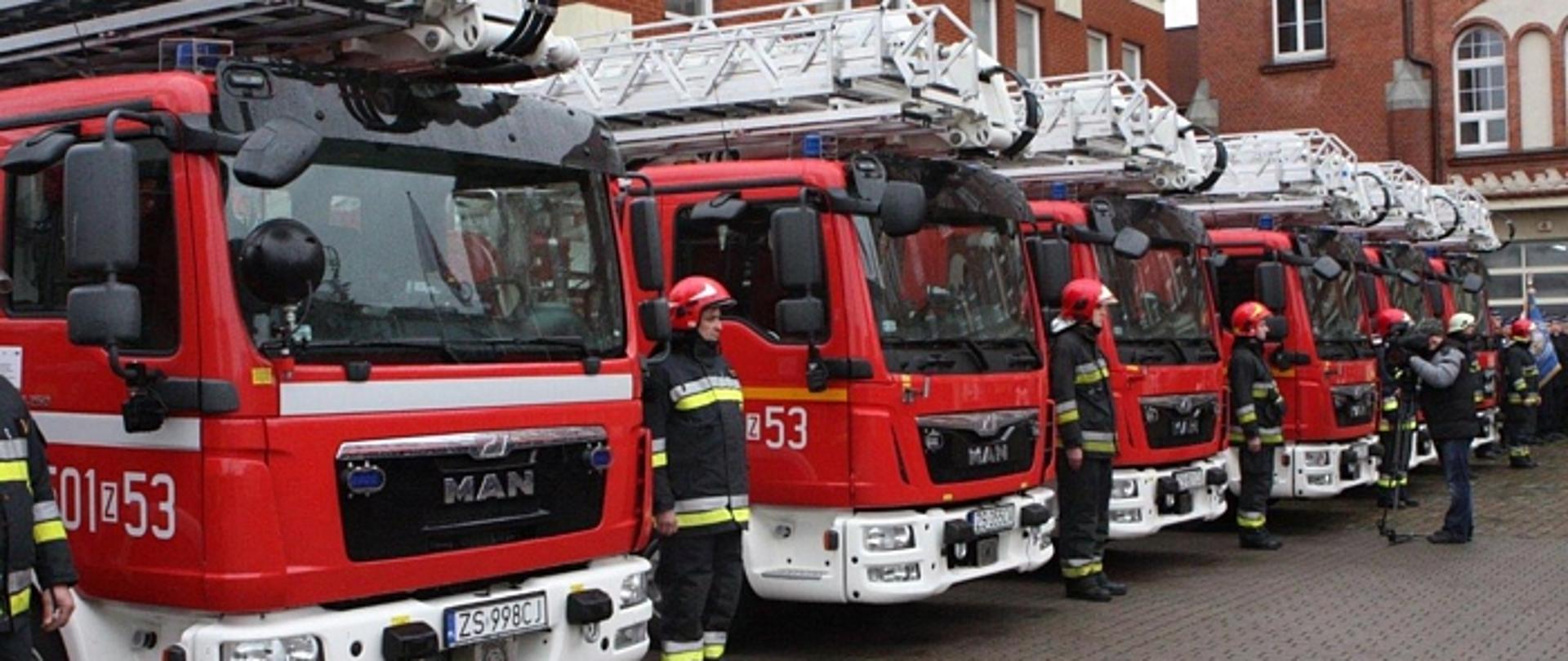 Zdjęcie przedstawia nowe samochody specjalne z podnośnikiem oraz stojących przy nich strażakach