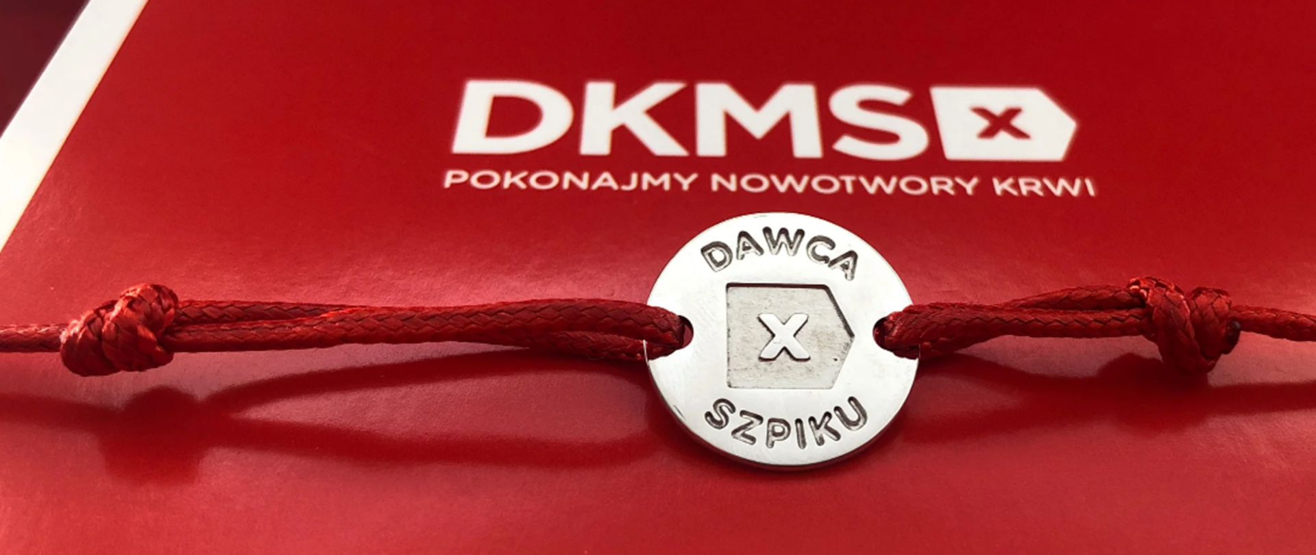 Na czerwonym tle z napisem DKMS ozdobny krążek z napisem Dawca Szpiku