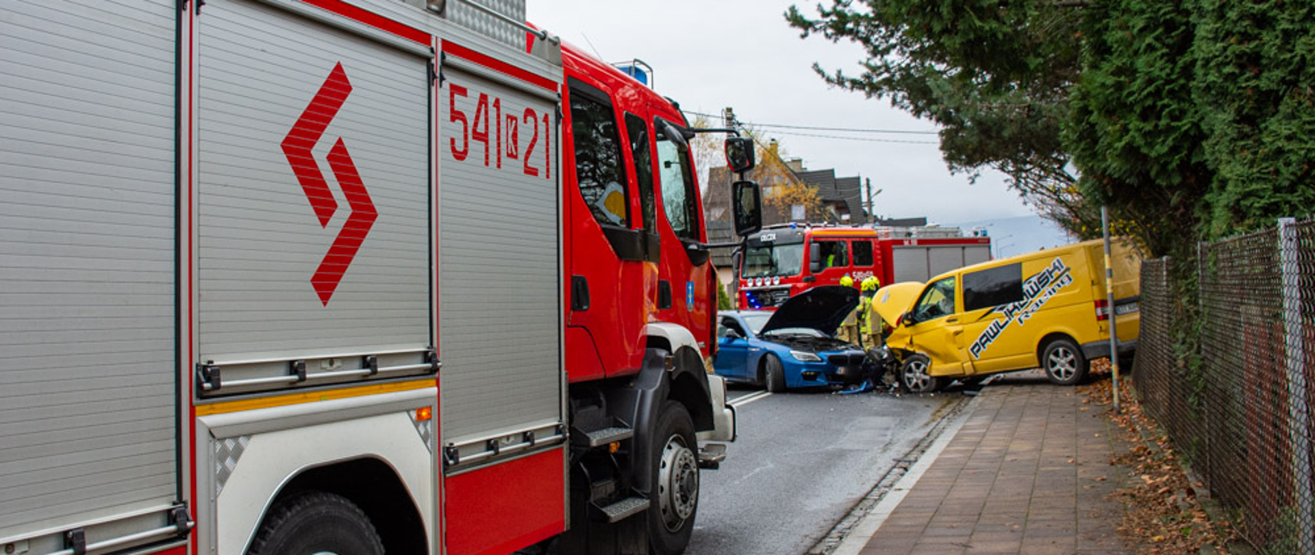 Zdjęcie przedstawia skutek wypadku drogowego do którego doszło w Zakopanem na ul. Wojdyły. W zdarzeniu brały udział dwa pojazdy. Bus i samochód osobowy. Na pierwszym planie znajduje się, wóz strażacki z Jednostki ratowniczo-gaśniczej w Zakopanem, w tle rozbite samochody oraz drugi wóz strażacki zabezpieczający miejsce zdarzenia.