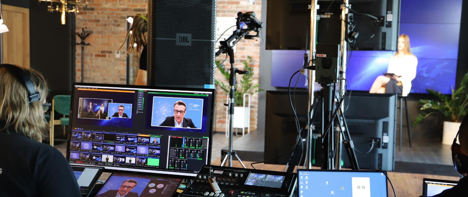 Widok reżyserki webinaru. Na ekranach, przed którymi siedzi realizator - Krzysztof Szubert, w tle dwoje prowadzących.