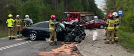 Samochód osobowy z uszkodzonym przodem blokujący drogę, w tle pojazdy służb ratowniczych
