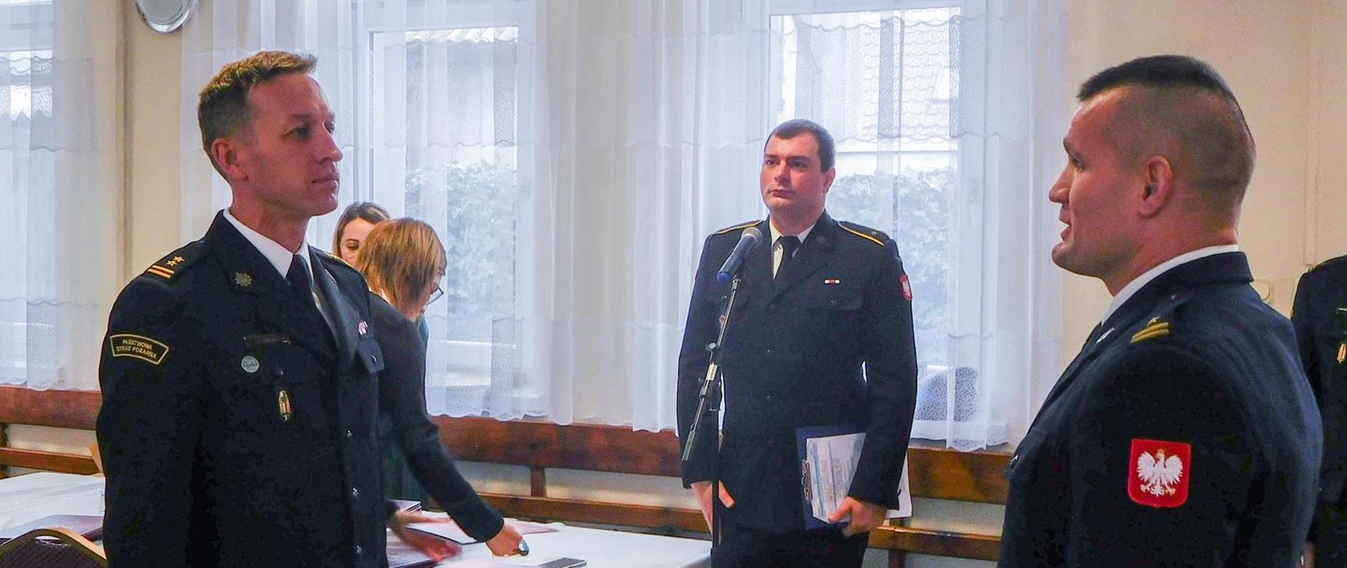 składanie meldunku strażakowi przez innego strażaka w tle stoi na baczność strażak