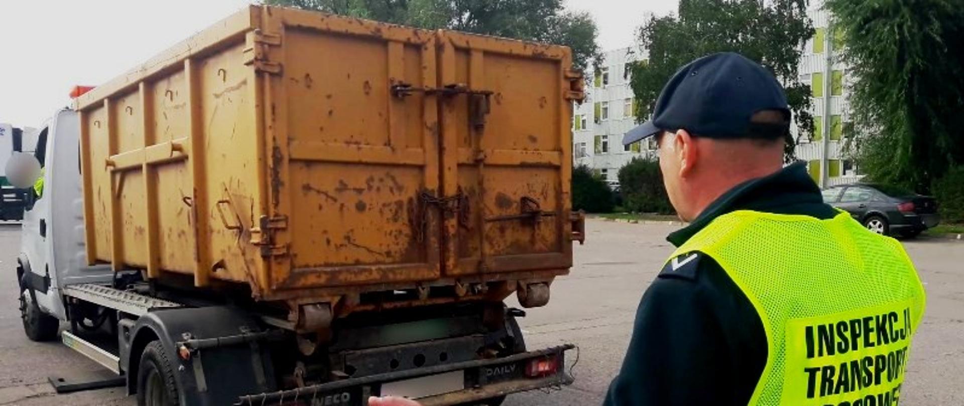 Inspektor ITD w kamizelce odblaskowej stoi za samochodem typu bus z żółtym kontenerem na odpady.