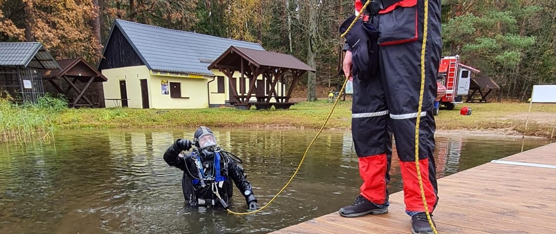 Zdjęcie obrazuje nurka wchodzącego do wody w tle budynki.