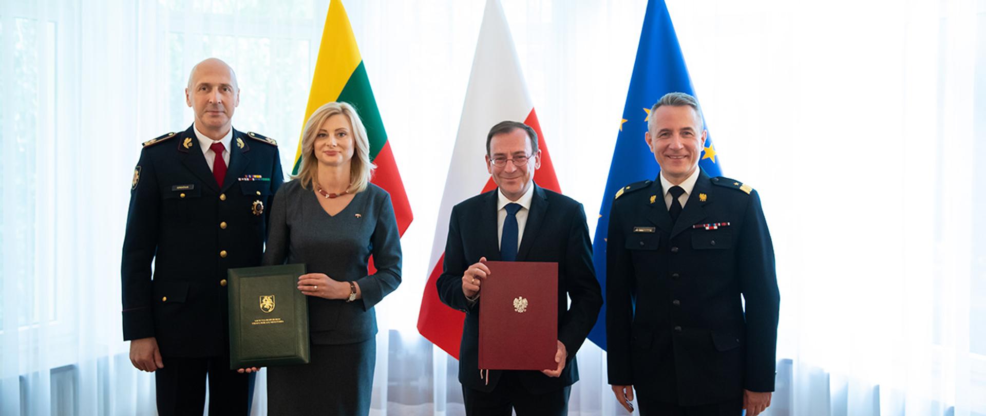 Na zdjęciu widać Mariusza Kamińskiego ministra SWiA, Ritę Tamašunienė minister SW Litwy trzymających swoje podpisane Memoranda. Obecni są również Andrzej Bartkowiak, komendant główny Państwowej Straży Pożarnej i Saulius Greičius, kierownik Straży Pożarnej Litwy. W tle widać flagi Polski, Litwy i UE.