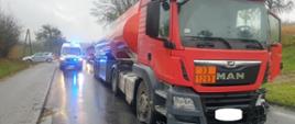 Zdjęcie przedstawia uszkodzoną cysternę na tle karetki pogotowia oraz radiowozu policyjnego.