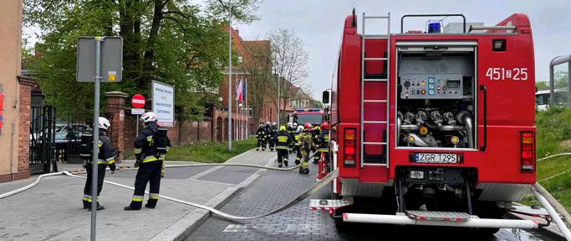 Zdjęcie przedstawia strażaków rozwijających linie wężowe.