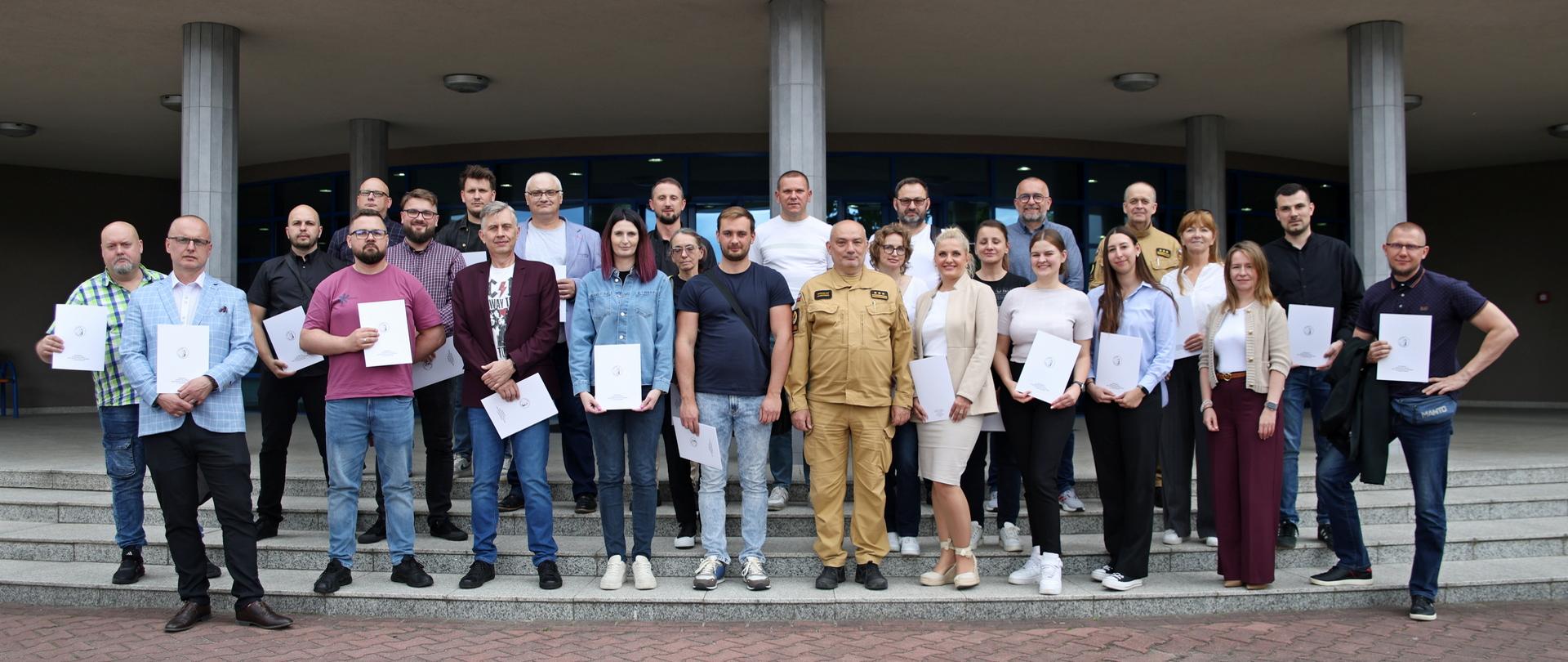 Pamiątkowe zdjęcie grupowe uczestników szkolenia inspektorów ochrony przeciwpożarowej (24 osoby) w towarzystwie Komendanta Centralnej Szkoły PSP, kobiety oraz oficera CS PSP