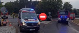 Zdjęcie ogólne na miejsce zdarzenia. Widok na skrzyżowanie na którym doszło do zdarzenia. Widać służby ratownicze i rozbite auta. Jest pochmurno. Na pierwszym planie karetka pogotowia.