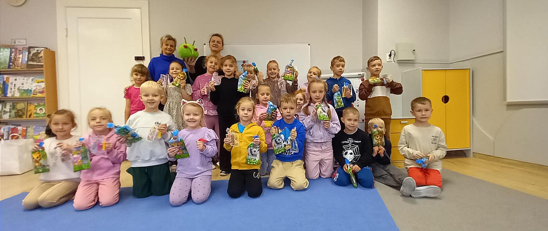 Grupa przedszkolaków wraz z dwiema kobietami uśmiechają się