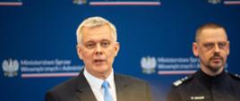 Minister Tomasz Siemoniak (po lewej) oraz komendant główny Policji gen. insp. Marek Boroń (po prawej) stoją na tle niebieskiej ścianki ze zmuliplikowanym logo MSWiA (orzeł, napis Ministerstwo Spraw Wewnętrznych i Administracji oraz biało-czerwony pasek). Przed ministrem widać dwa czarne mikrofony kierunkowe. 