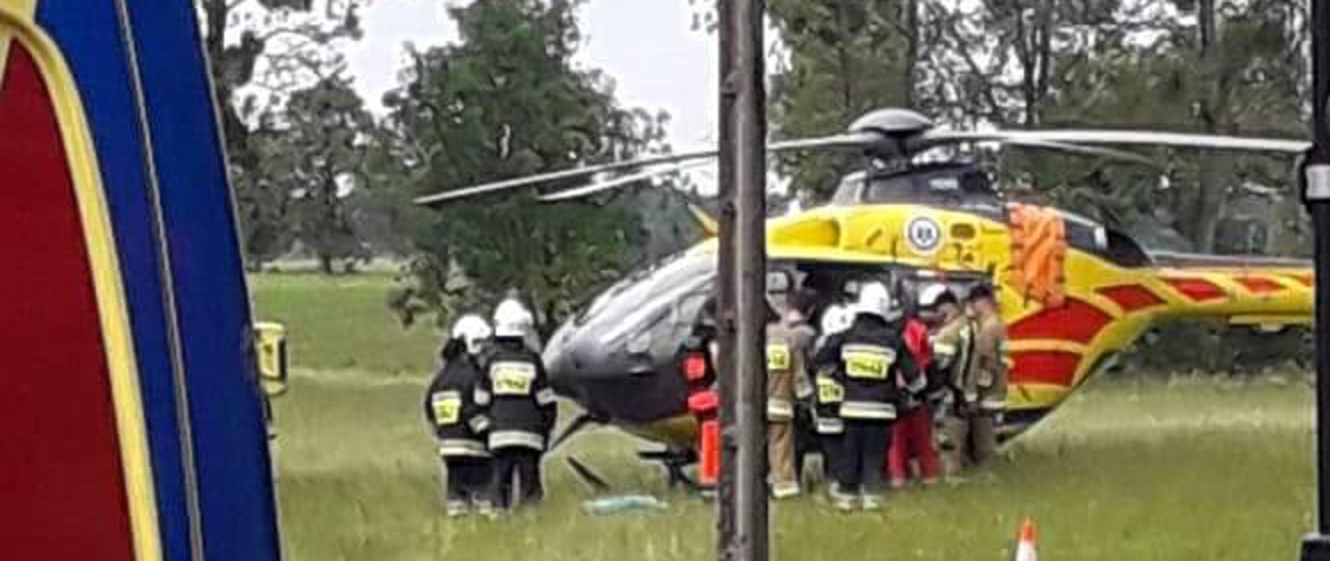 Śmigłowiec LPR stoi na łące, przy nim załoga i strażacy