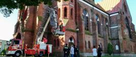 Zdjęcie przedstawia ćwiczenia strażaków przy kościele z udziałem podnośnika