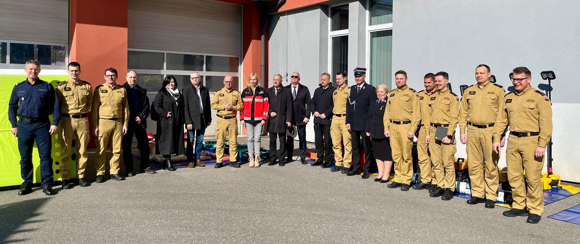 Funkcjonariusze i zaproszeni goście na tle zakupionego sprzętu na placu zewnętrznym Komendy