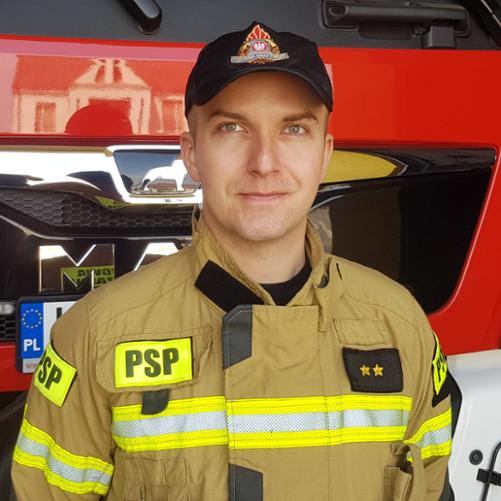 Portret strażaka w ubraniu specjalnym na tle samochodu pożarniczego