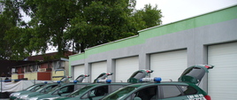 Zdjęcie przedstawia pięć oznakowanych radiowozów marki Opel Astra IV ustawionych w rzędzie przed garażami w Izbie Administracji Skarbowej w Olsztynie