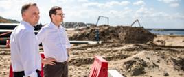 Premier Mateusz Morawiecki i prezydent Andrzej Duda stoją na tle terenu przekopu Mierzei Wiślanej.