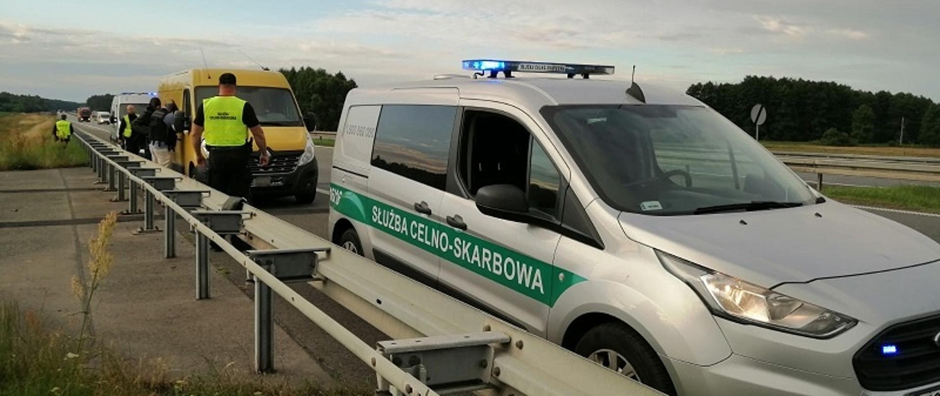 Na drodze funkcjonariusze, radiowóz Służby Celno-Skarbowej, samochód dostawczy.