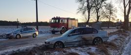 Na zdjęciu widać uszkodzony samochód osobowy stojący w poprzek jezdni, za nim znajdują się pojazdy służb ratowniczych.