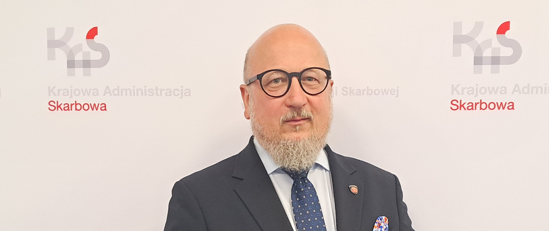 Mężczyzna na tle ściany z logo KAS i napisami Izba Administracji Skarbowej w Bydgoszczy