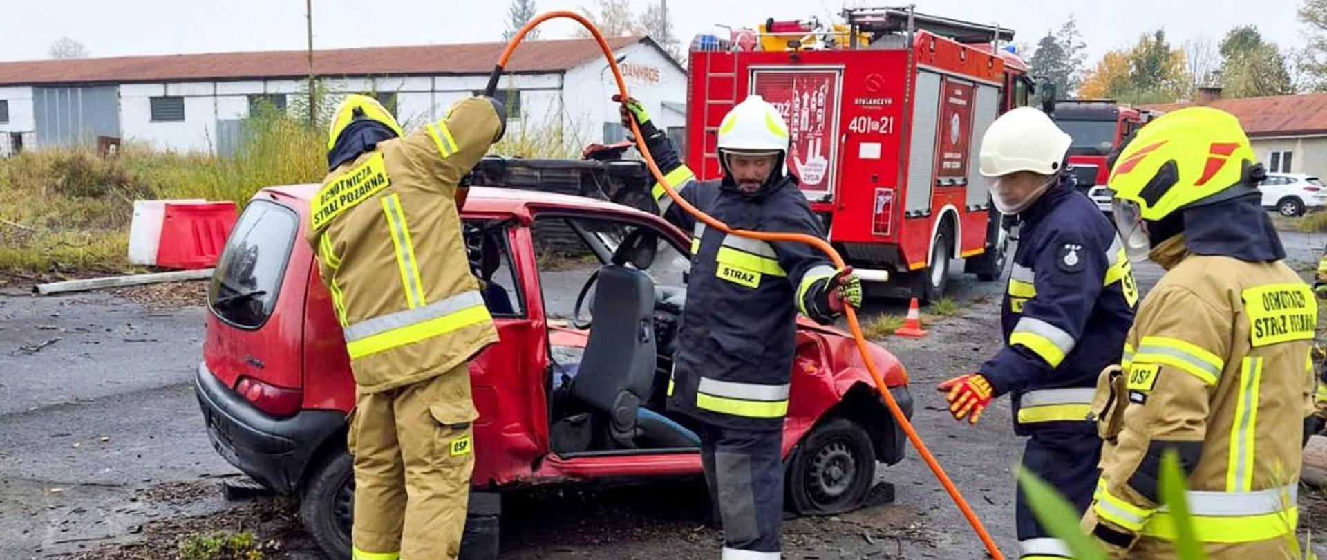 Zdjęcie przedstawia strażaków OSP przy samochodzie z wyciętymi drzwiami bocznymi. Strażacy operują narzędziami hydraulicznymi. 