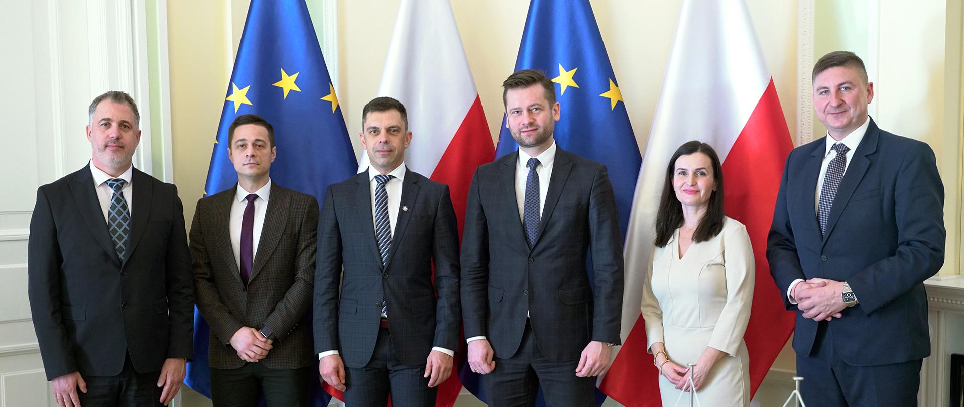 Minister Sportu i Turystyki Kamil Bortniczuk spotkał się ze swoim rumuńskim odpowiednikiem Carlem-Edouardem Novakiem. Na zdjęciu uczestnicy spotkania stoją na tle flag Polski i Unii Europejskiej.