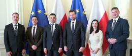 Minister Sportu i Turystyki Kamil Bortniczuk spotkał się ze swoim rumuńskim odpowiednikiem Carlem-Edouardem Novakiem. Uczestnicy spotkania stoją na tle flagi Polskiej i Unii Europejskiej.