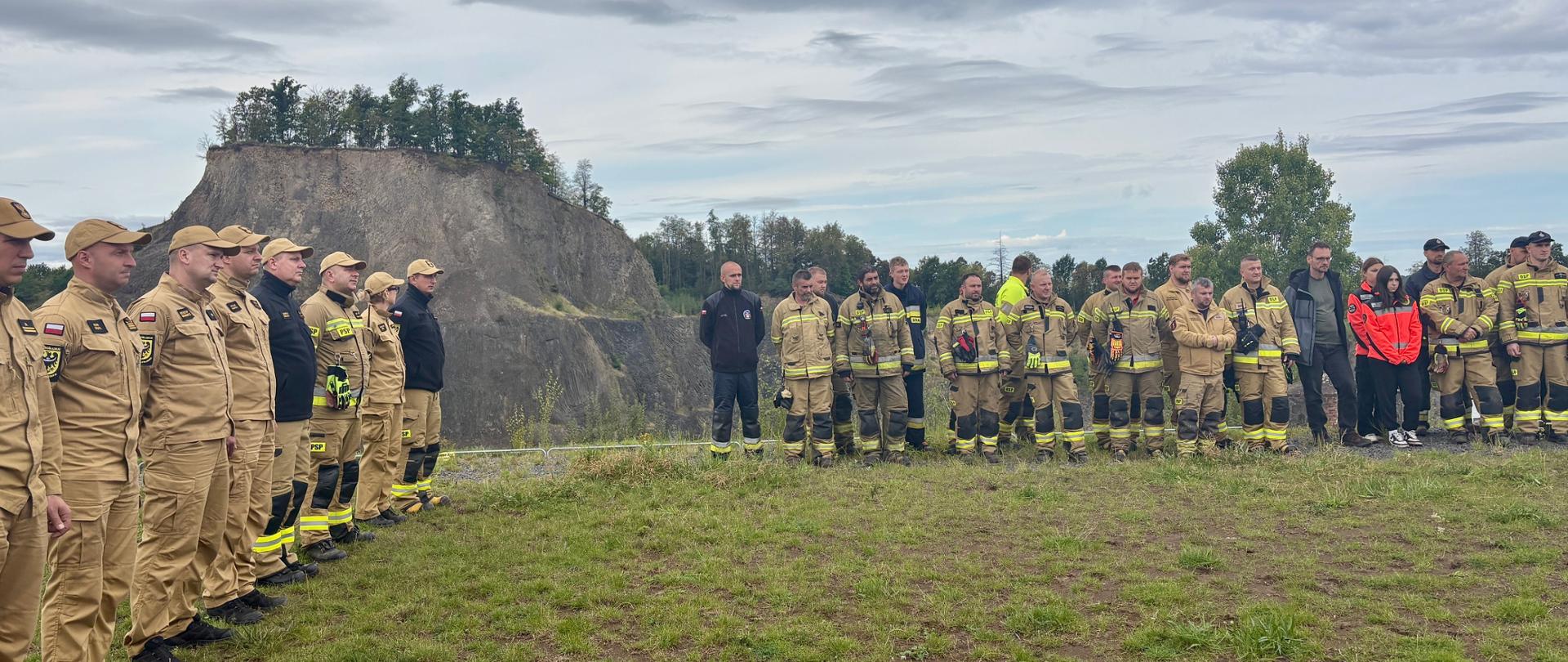 strażacy stoją na zbiórce, w tle Wilcza Góra