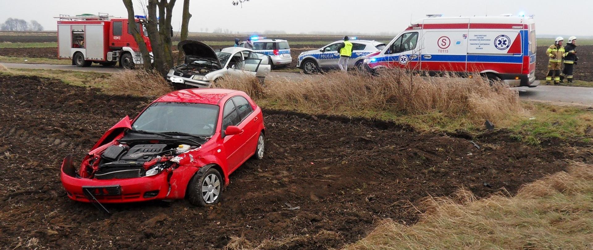 Zdjęcie przedstawia uszkodzone pojazdy w tle pojazdy straży pożarnej, policji i pogotowia. 