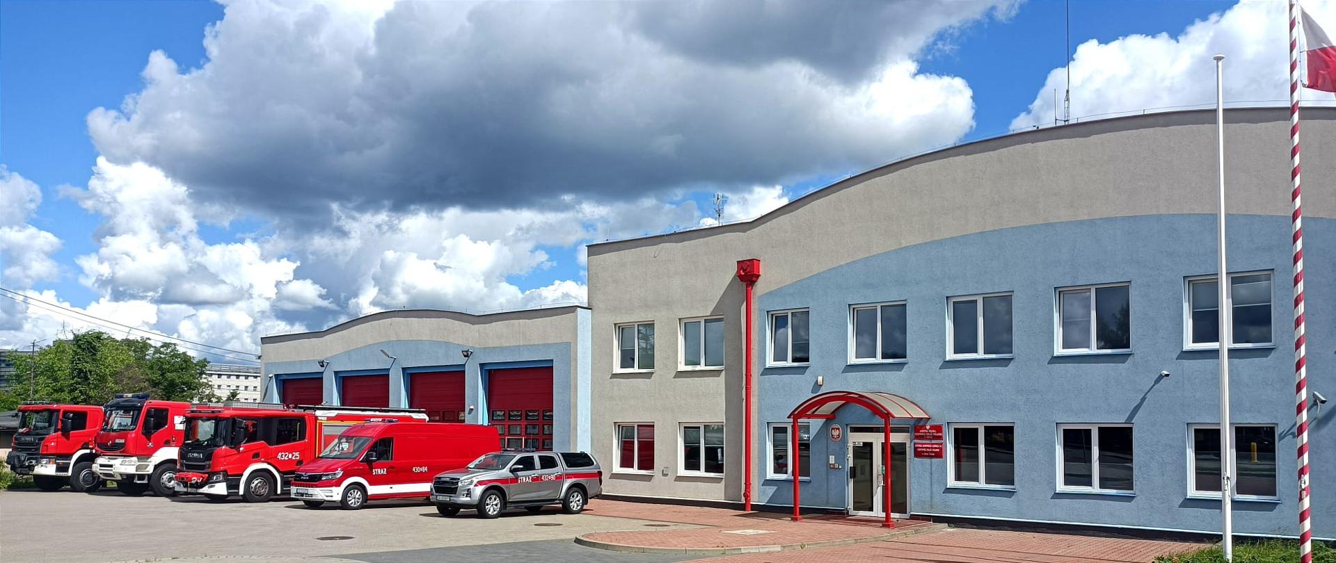 Biało niebieski budynek Jednostki ratowniczo gaśniczej numer 2 Gdynia Chylonia. Przed nim wystawione samochody strażackie.