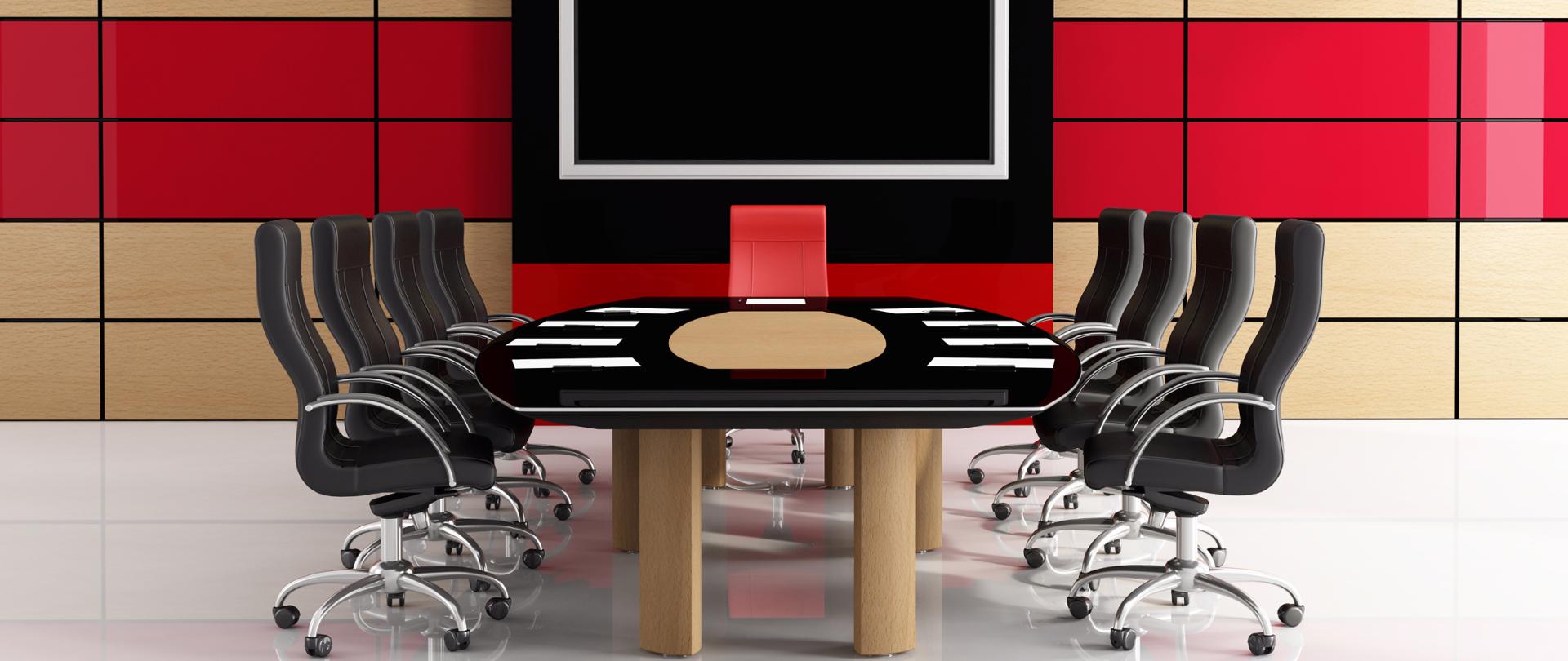W centrum biurko a wokół czarne krzesła i jedno czerwone 