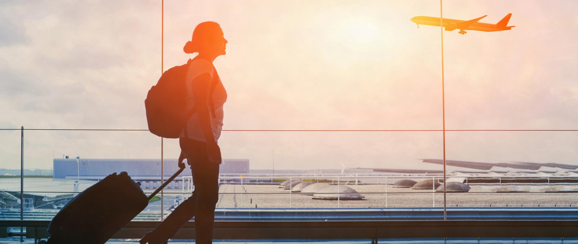 Turystka z bagażem podręcznym i plecakiem maszeruje po porcie lotniczym