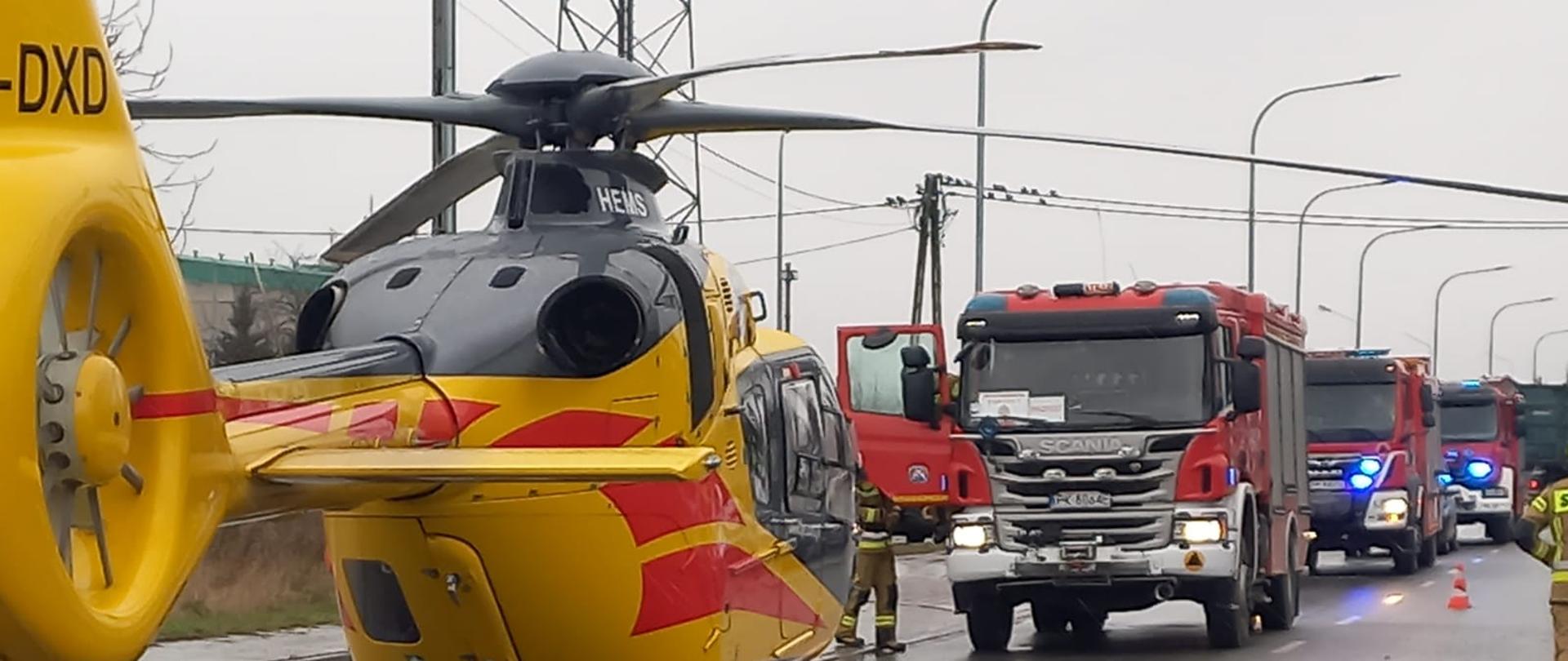 Zdjęcie wykonane w ciągu dnia. Zachmurzenie duże. Widać samochody ratowniczo-gaśnicze. Pojazdy są w kolorze czerwonym. Posiadają sygnalizację ostrzegawczą. Zdjęcie wykonane na drodze publicznej.