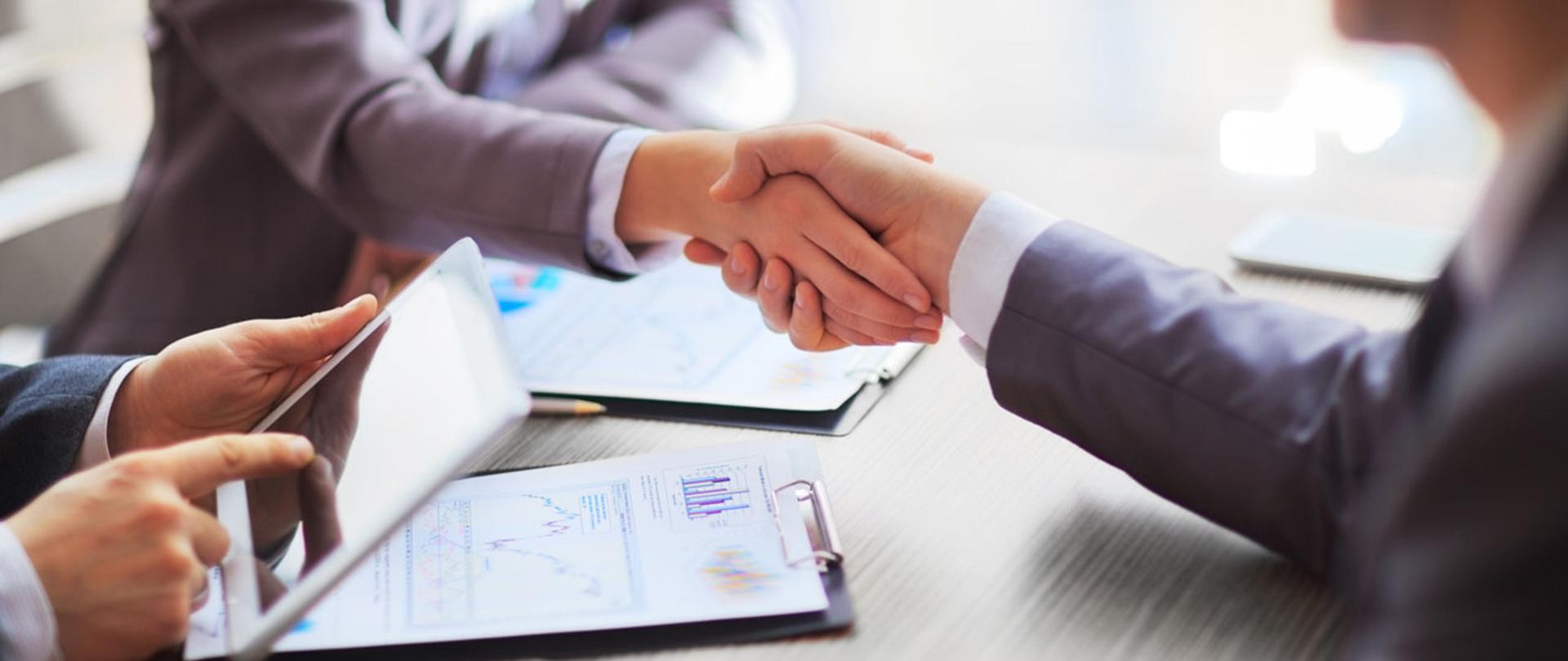 Podane ręce nad stołem, dłonie osoby pracującej na tablecie.