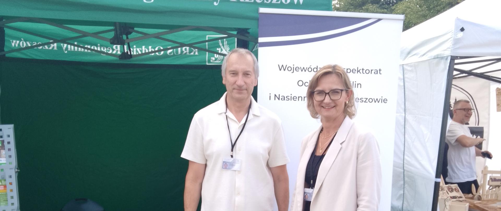 Dwie osoby stojące na tle zielonego namiotu. Mężczyzna i kobieta. W tle granatowo biały baner.